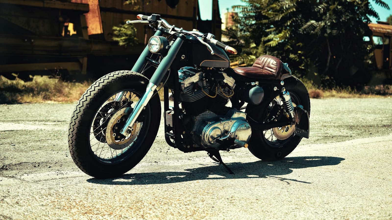 A custom bobber motorcycle with a plain unbranded tank parked outdoors near an old rail car, no rider, plate, or logo visible.