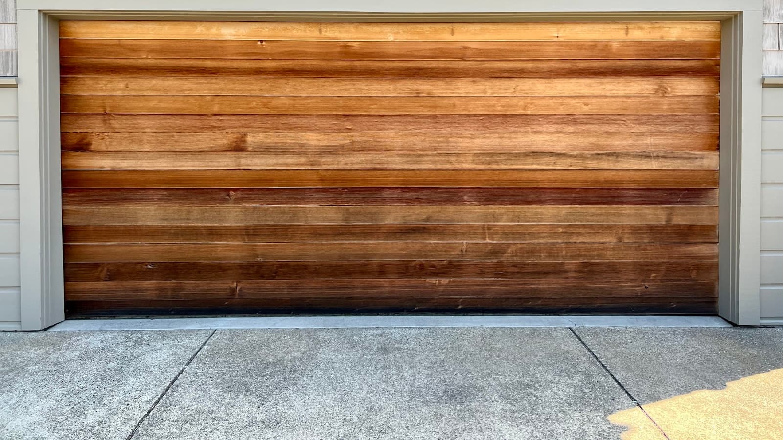 A clean, natural wood-toned garage door set into a shingled house exterior, with no people, text, or logos visible.
