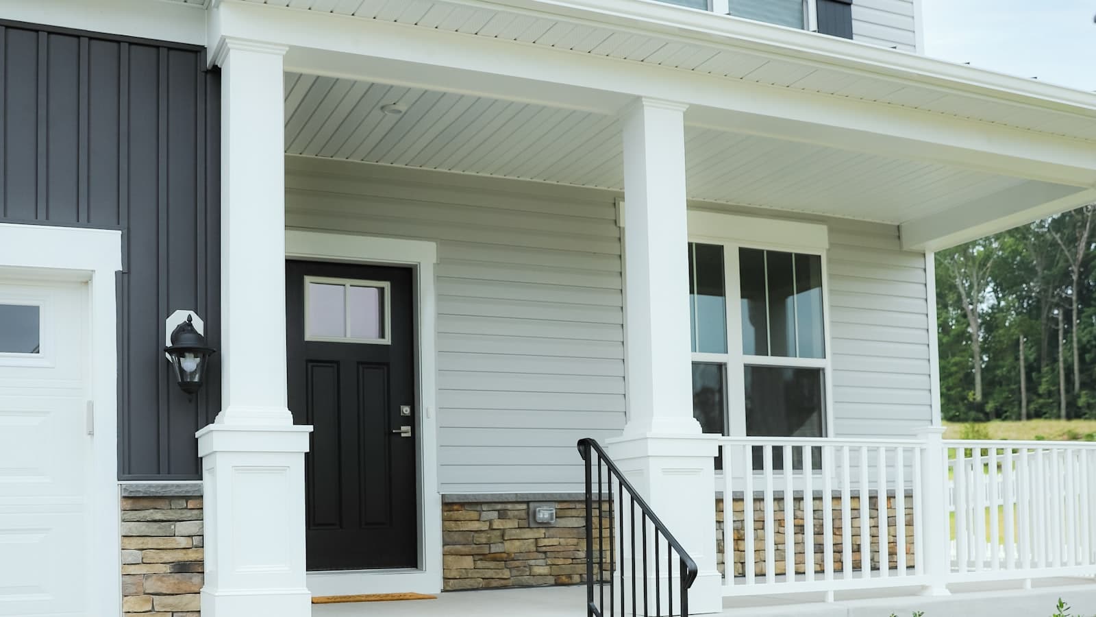 Close-up of a house's front porch showing light gray vinyl lap siding with a dark front door, no people or logos.