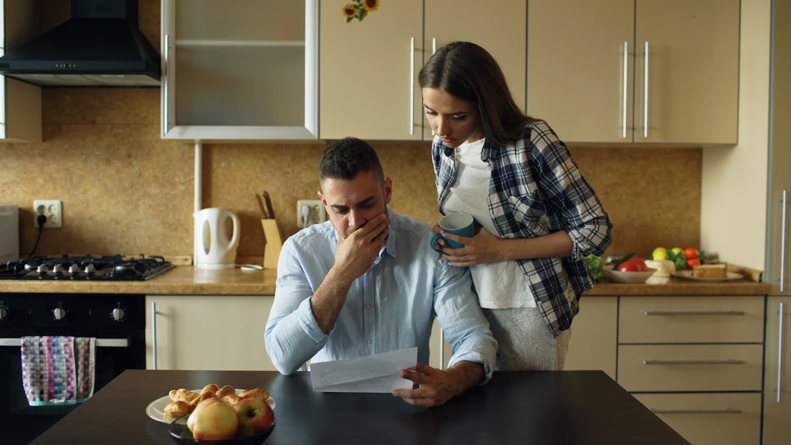 A couple in a kitchen looking stressed while reading an unpaid bill.
