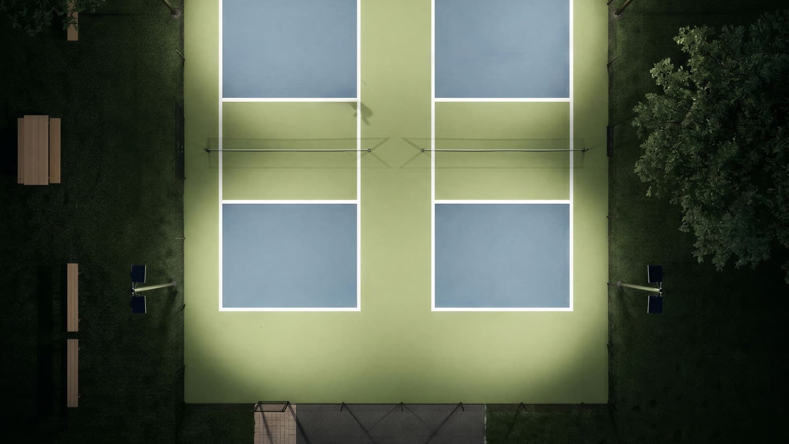 An aerial view of illuminated pickleball courts at night, surrounded by trees.