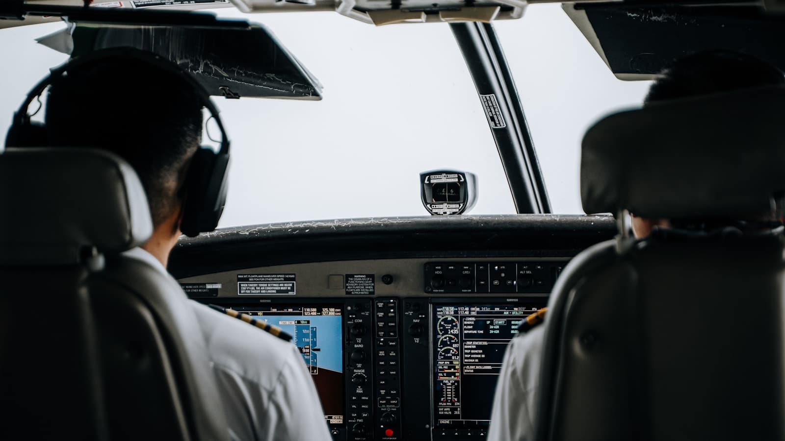 Two pilots seen through the cockpit doorway operating switches.