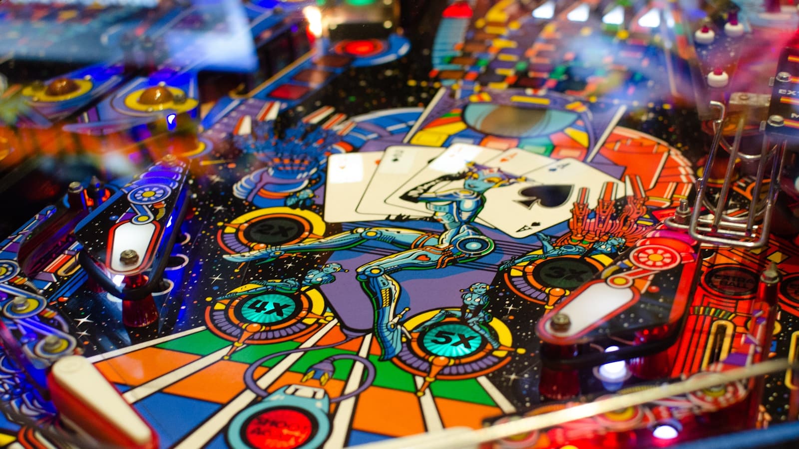 Close-up of a brightly lit, colorful pinball machine playfield with playing-card artwork.