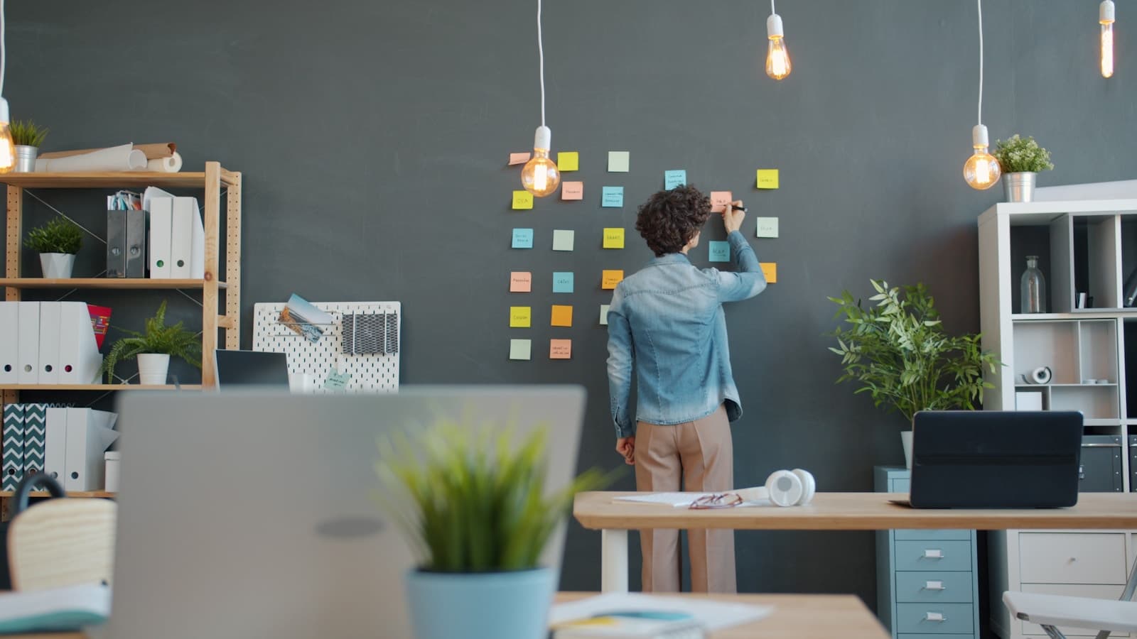 A person arranging colorful sticky notes in a grid on a dark wall, project-planning feel.