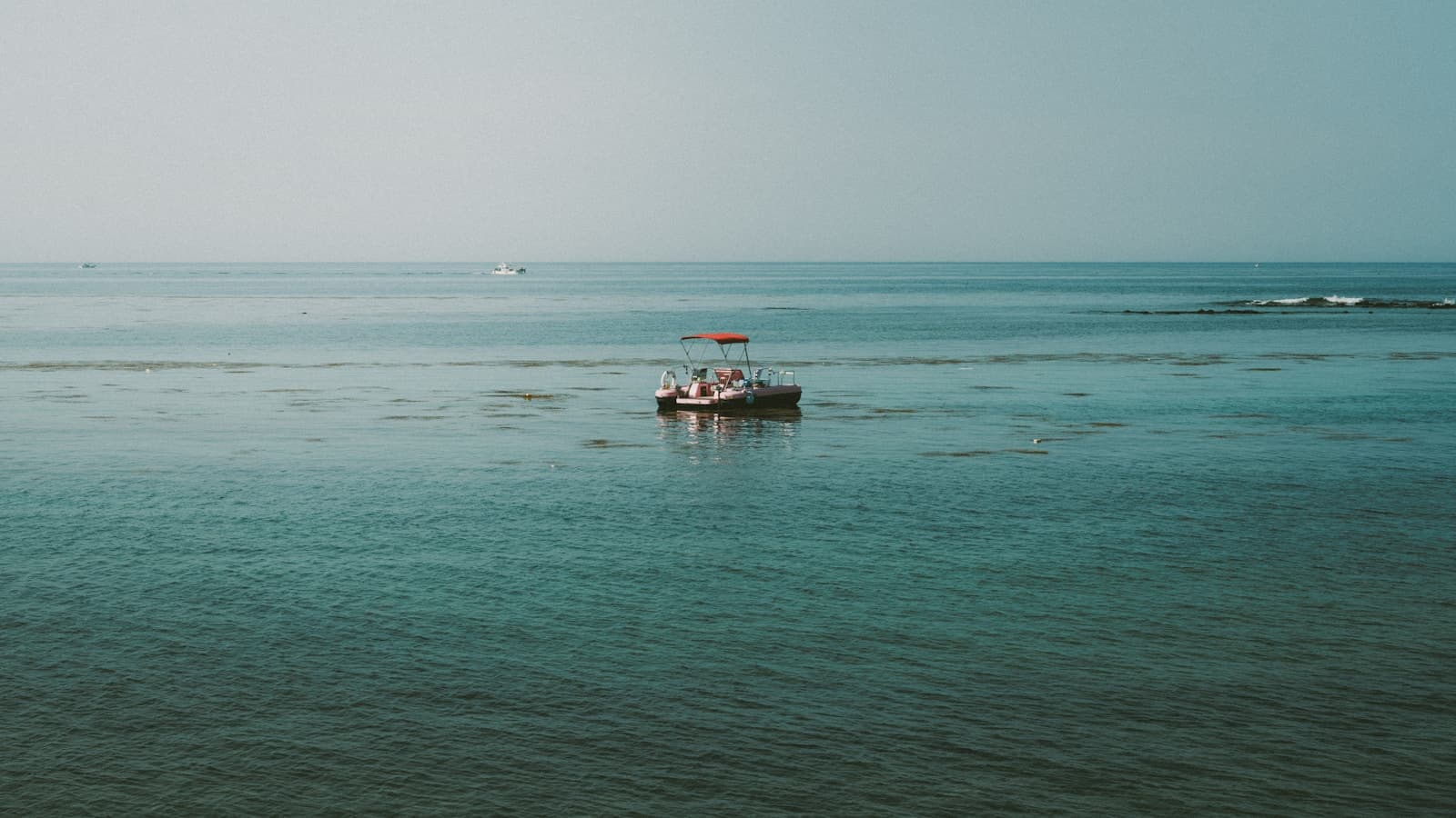 A pontoon boat with a red canopy sitting on calm turquoise open water, seen from above.