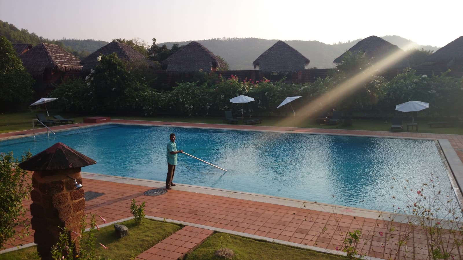 A pool technician skimming a resort-style pool with a long-handled net.