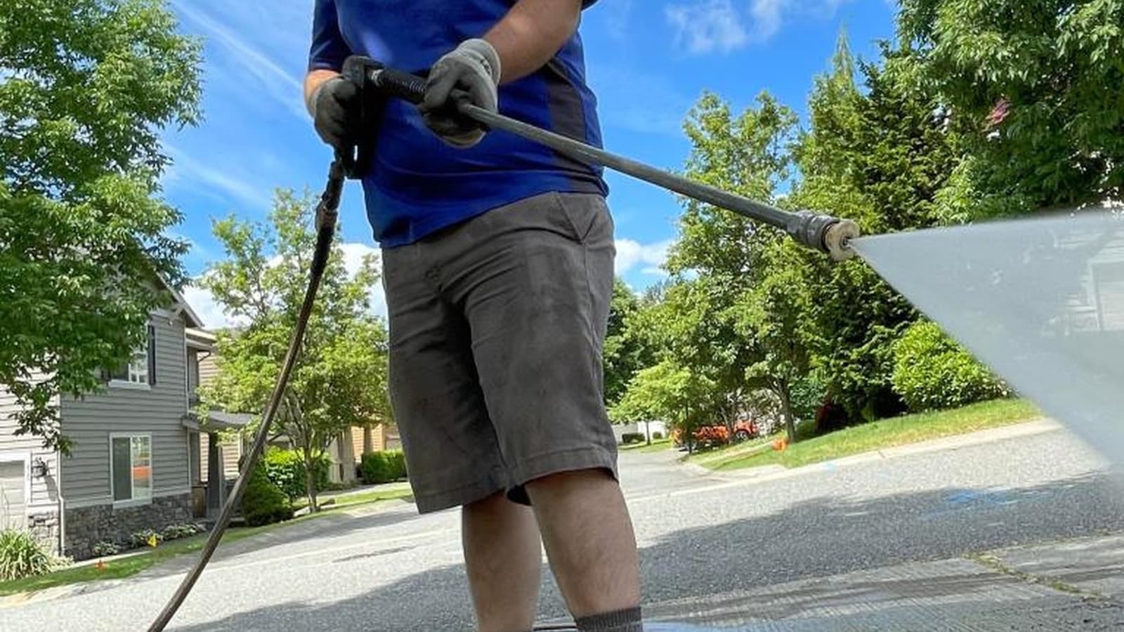 A man pressure-washing a residential driveway, low angle, blue sky.