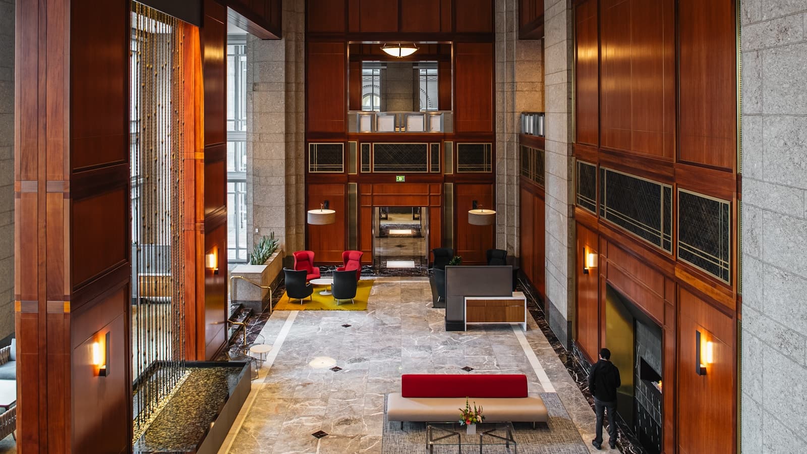 A grand wood-paneled lobby with marble floor, fireplace, and red leather seating.