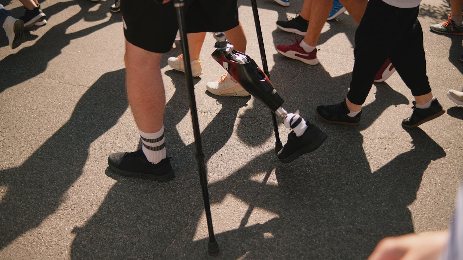 A person with a prosthetic leg walking with crutches among a group outdoors.
