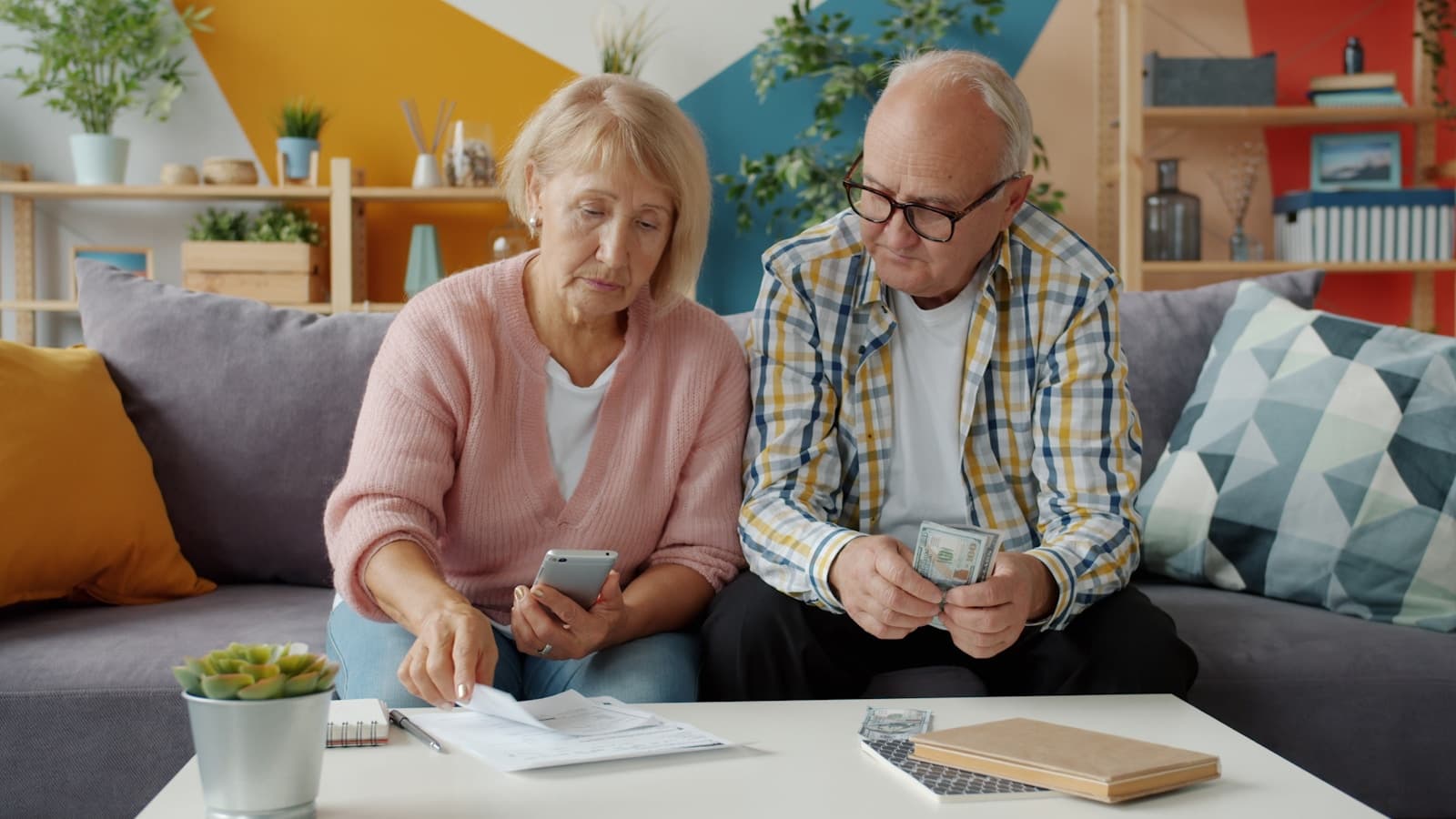 An elderly couple looking over bills and a phone together at home.