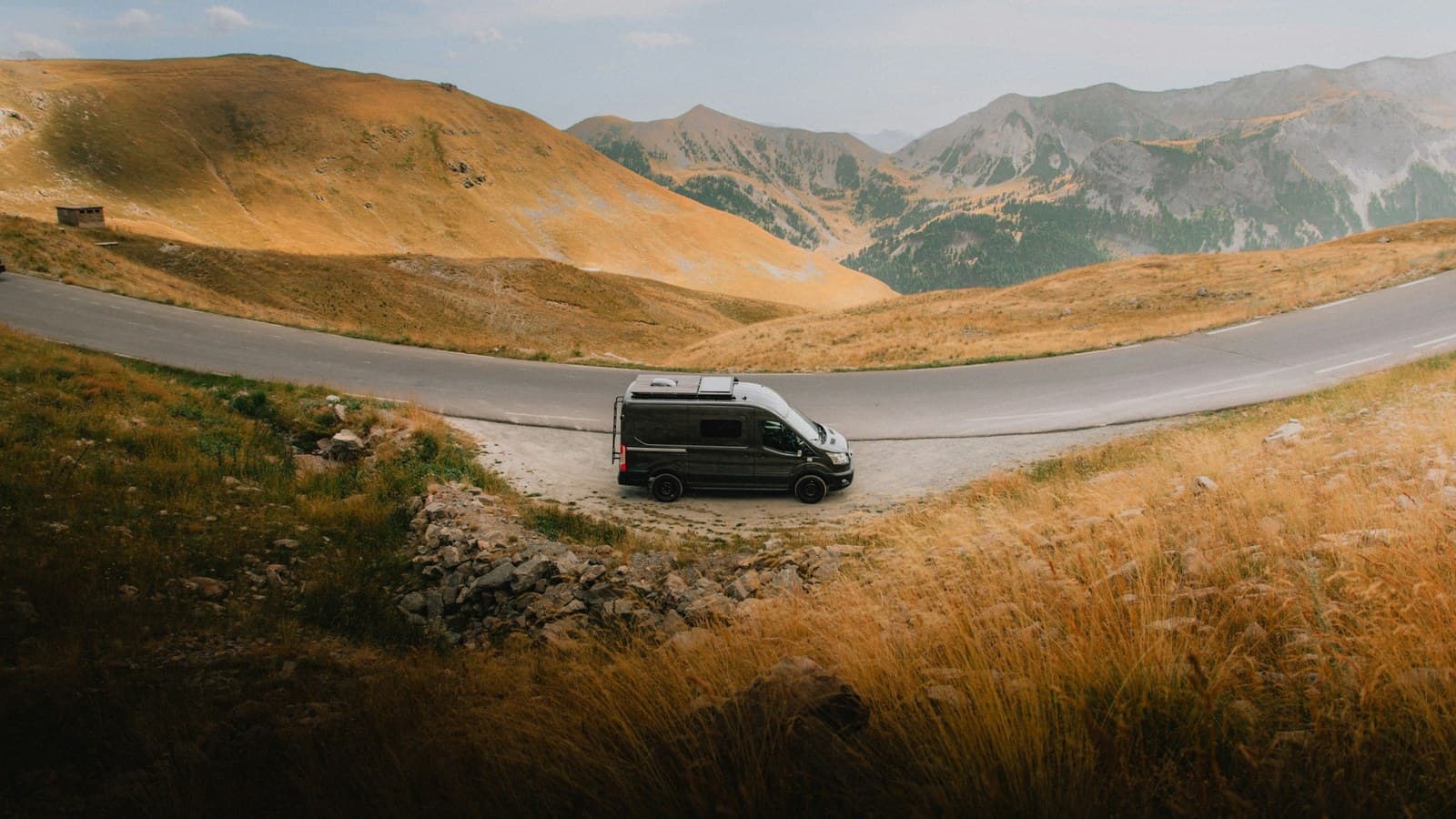 A van driving along a winding mountain road through green alpine scenery.
