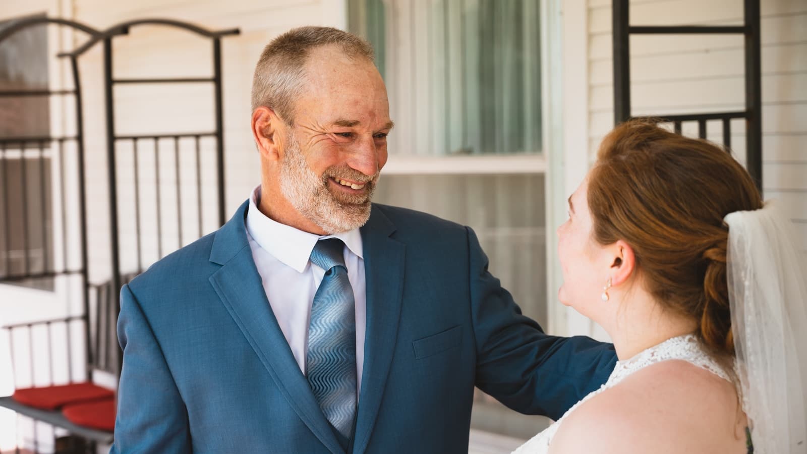 A silver-haired groom smiling warmly with his bride on a porch.