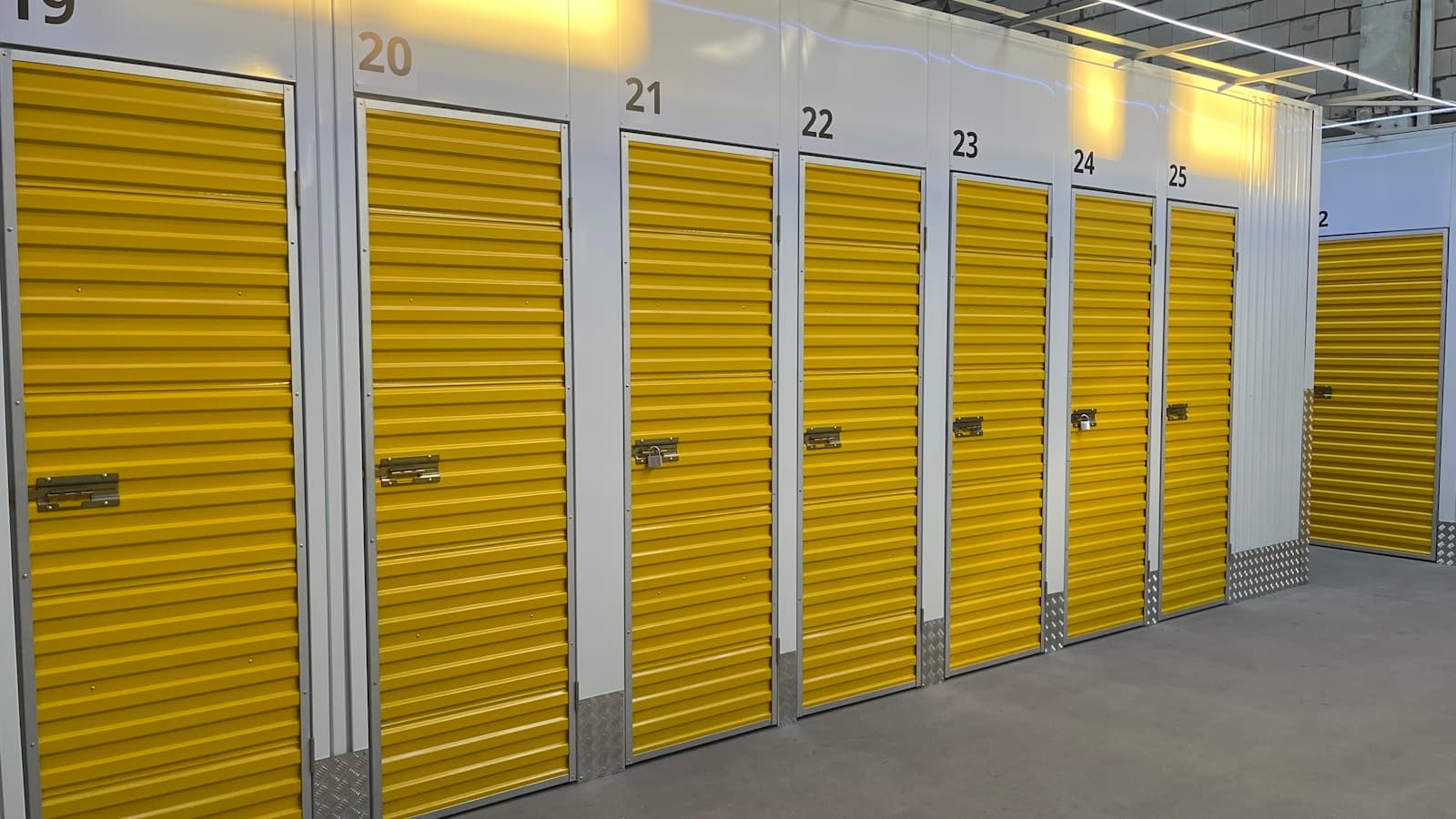 A row of bright yellow roll-up storage unit doors with only unit numbers.