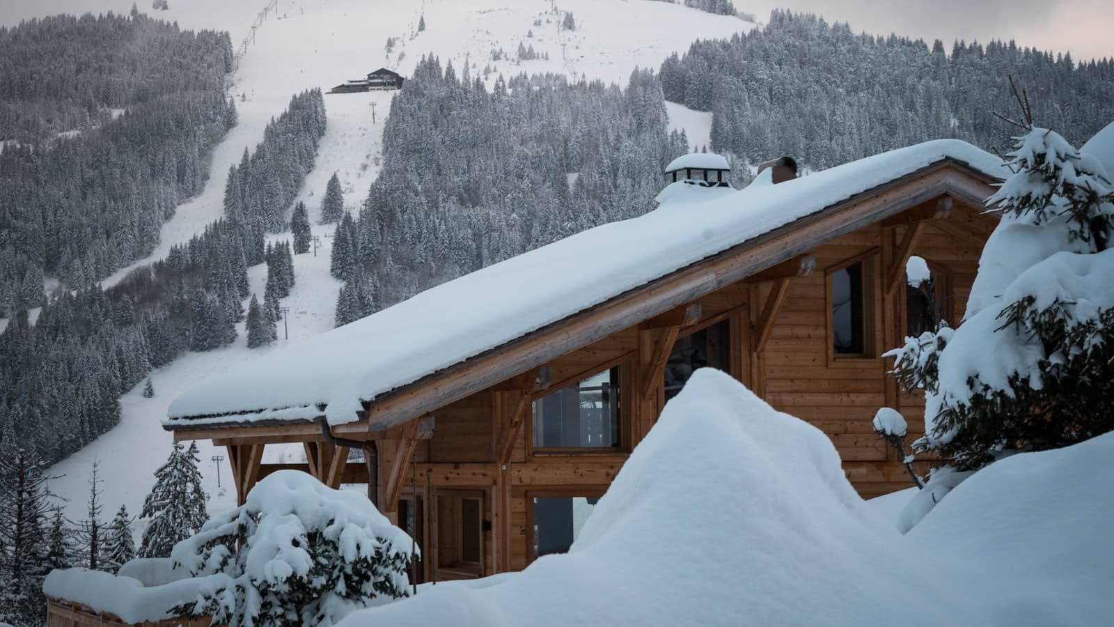 A snow-covered wooden ski chalet with a snowy mountain and ski slope in the background, no people, text, or logos.