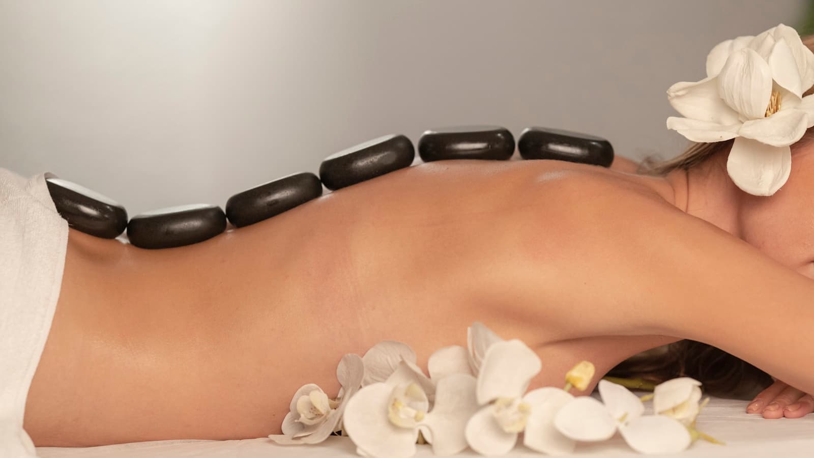 A hot stone massage on a person's back with white orchid petals.