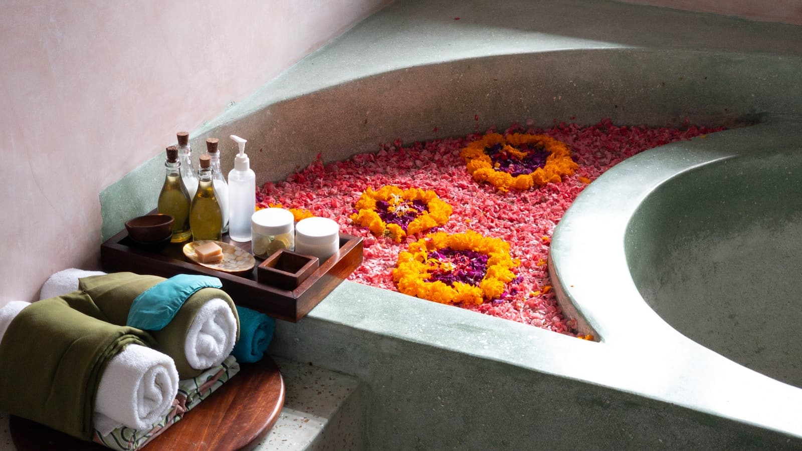 A flower-petal soaking tub with rolled towels and oils, spa-resort feel.