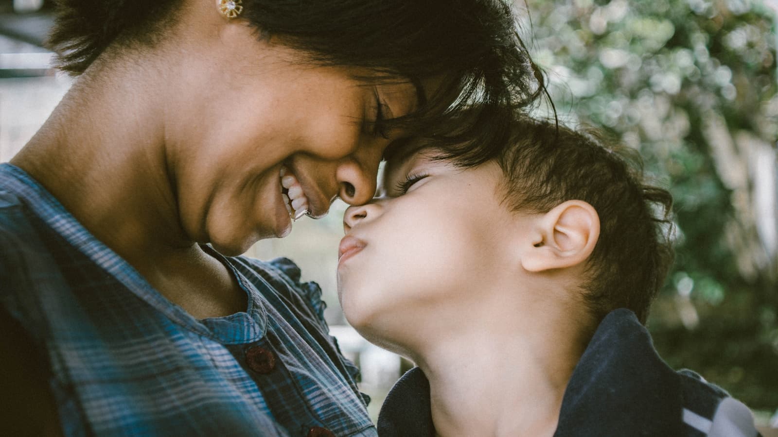 A mother and young son sharing a tender close moment outdoors.