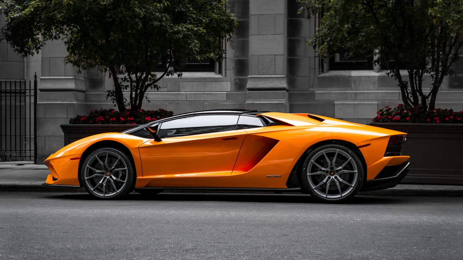 An orange Lamborghini Aventador shown in side profile on a city street, with no legible plate or brand text.