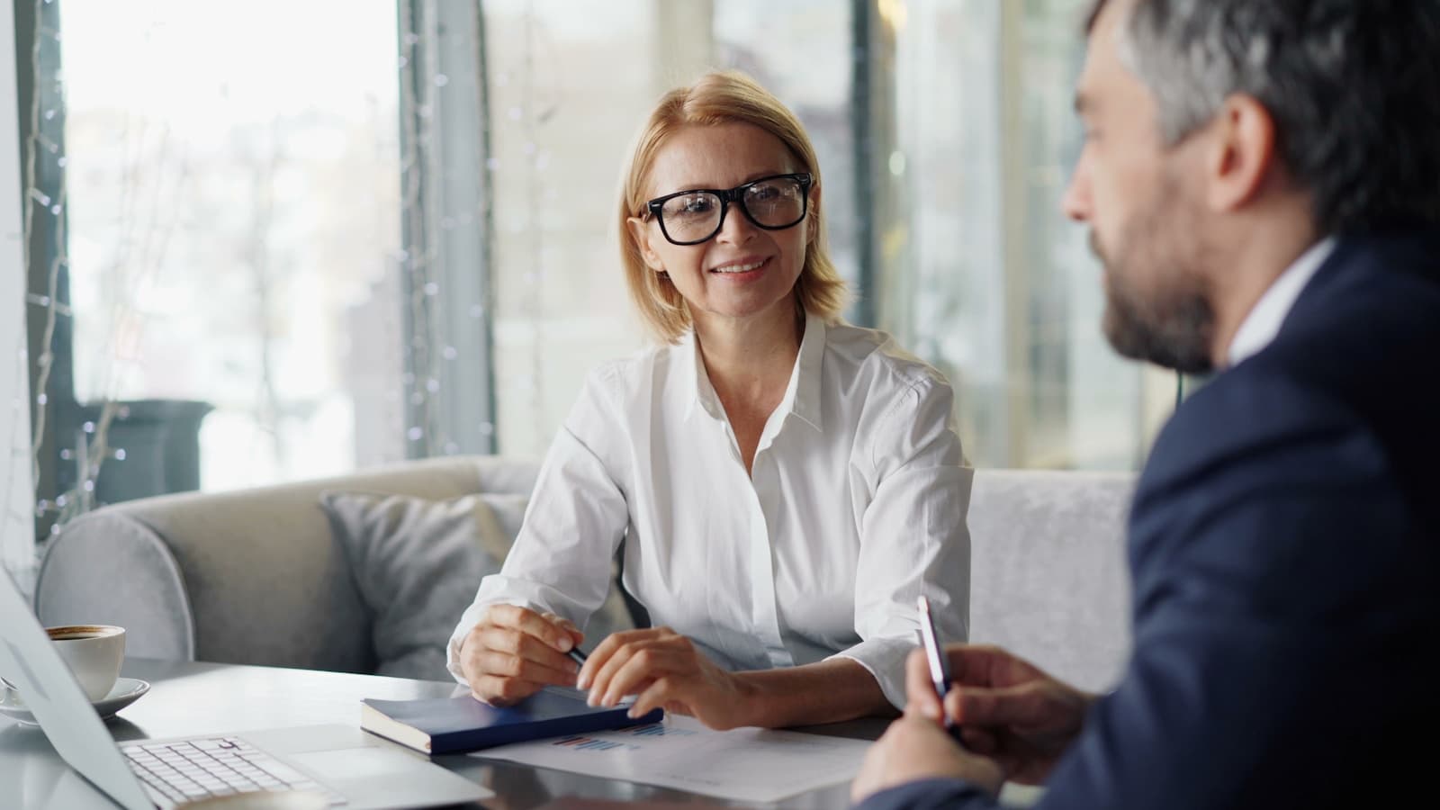 An advisor and couple in business attire reviewing documents, bright office.
