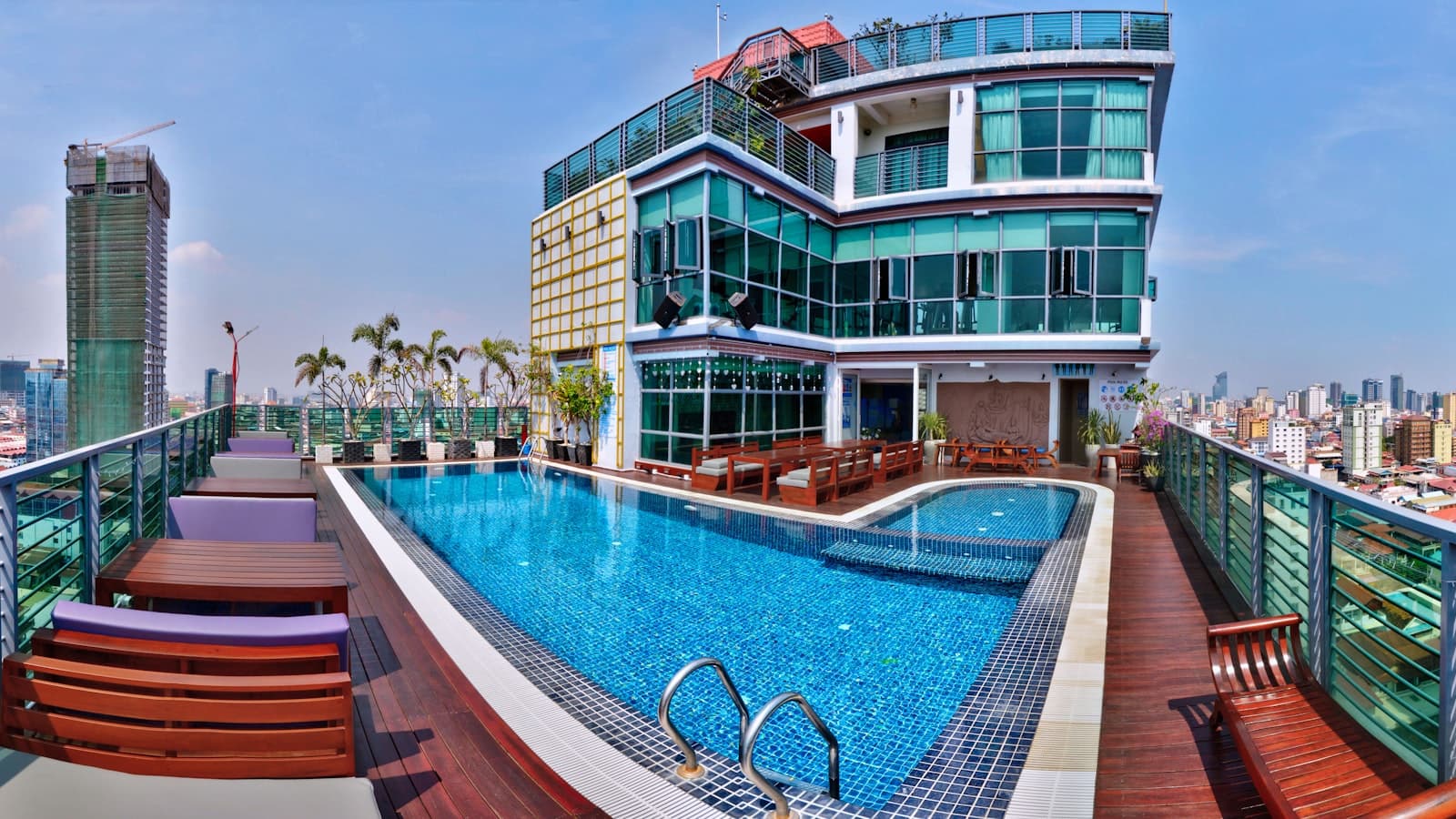 A rooftop resort swimming pool with lounge furniture and a city skyline behind it, no people and no legible signage of consequence.
