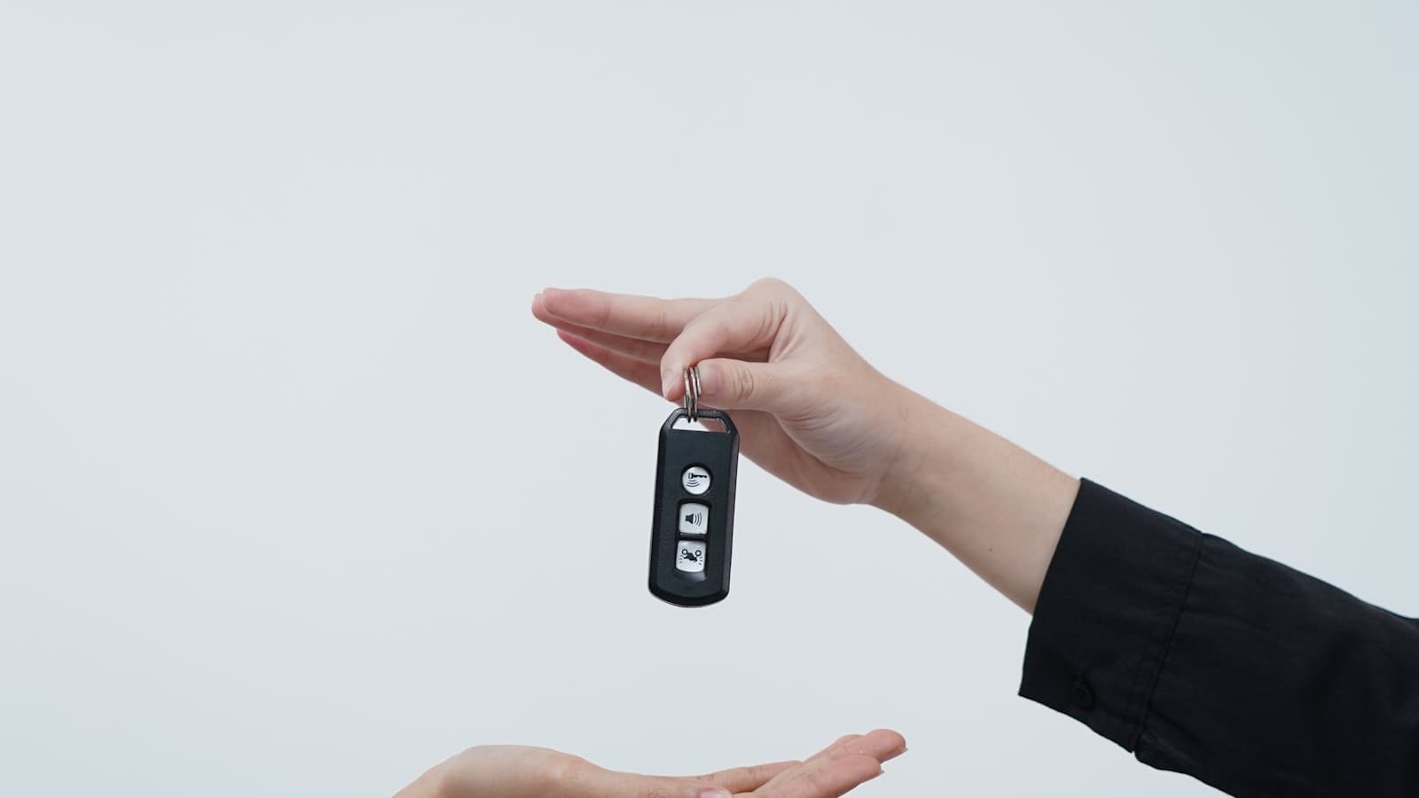 Two hands mid-exchange of a car key fob against a plain light background.