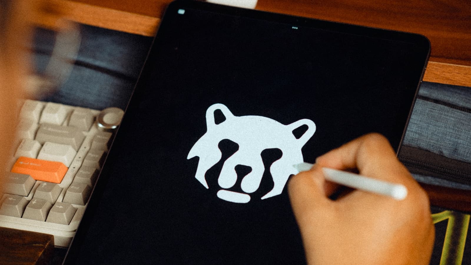 A hand drawing a bear-head logo on a tablet screen.