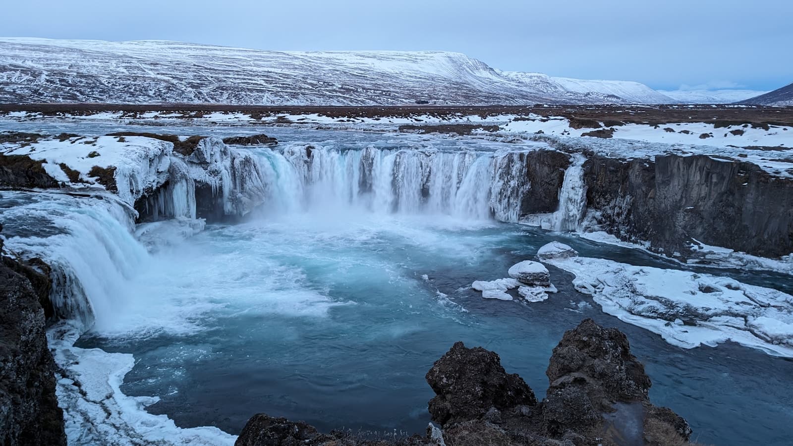 A frozen Icelandic waterfall with snow-covered highlands.