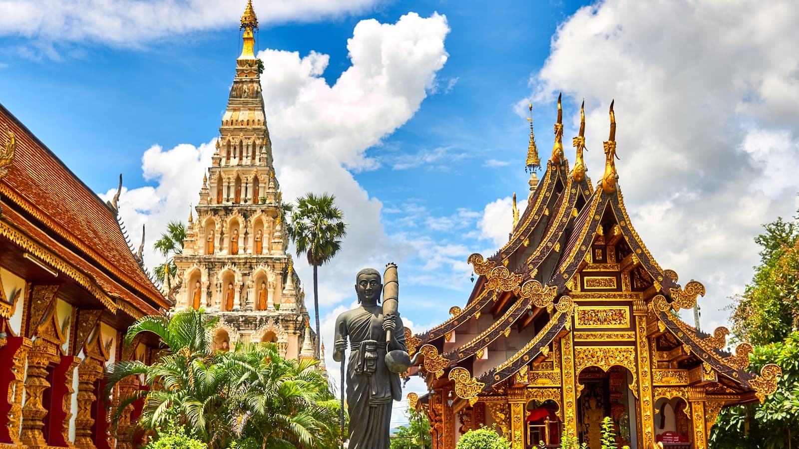 An ornate golden Thai temple with a standing Buddha statue against a blue sky.