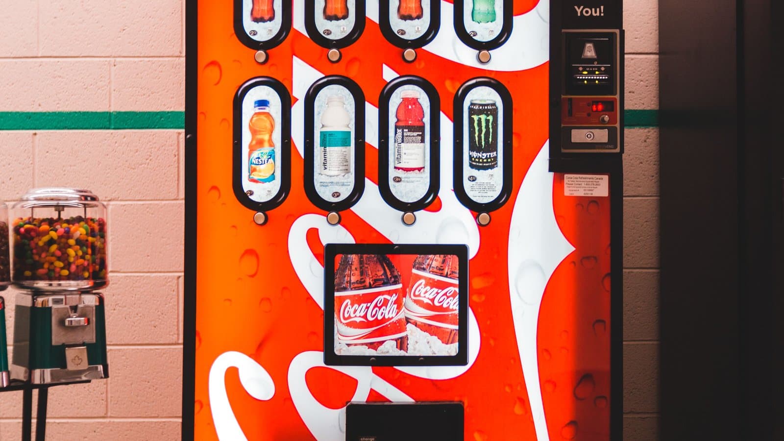 A row of colorful drink and snack vending machines inside a building interior.