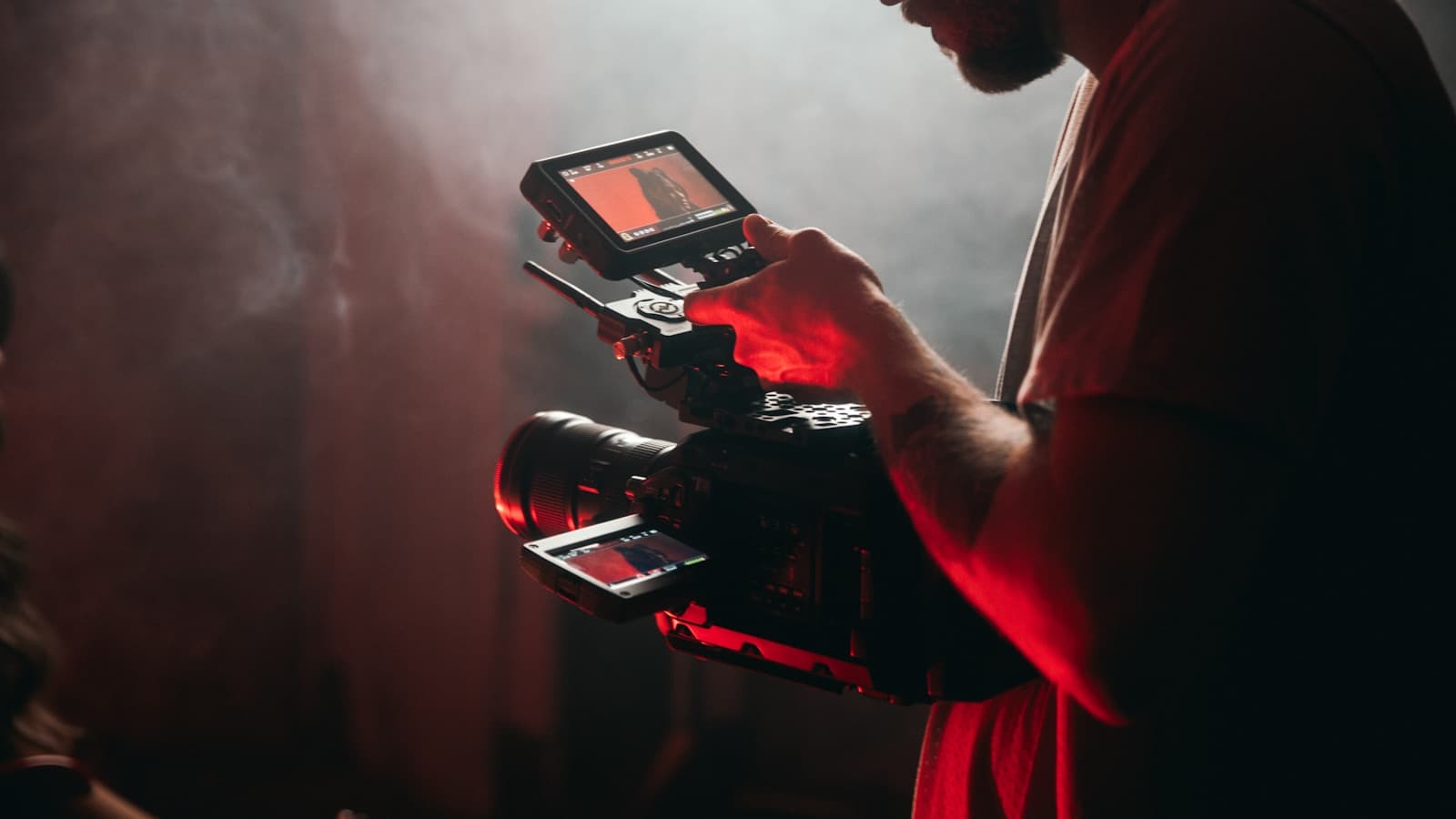 A man in a white t-shirt holding a black video camera.