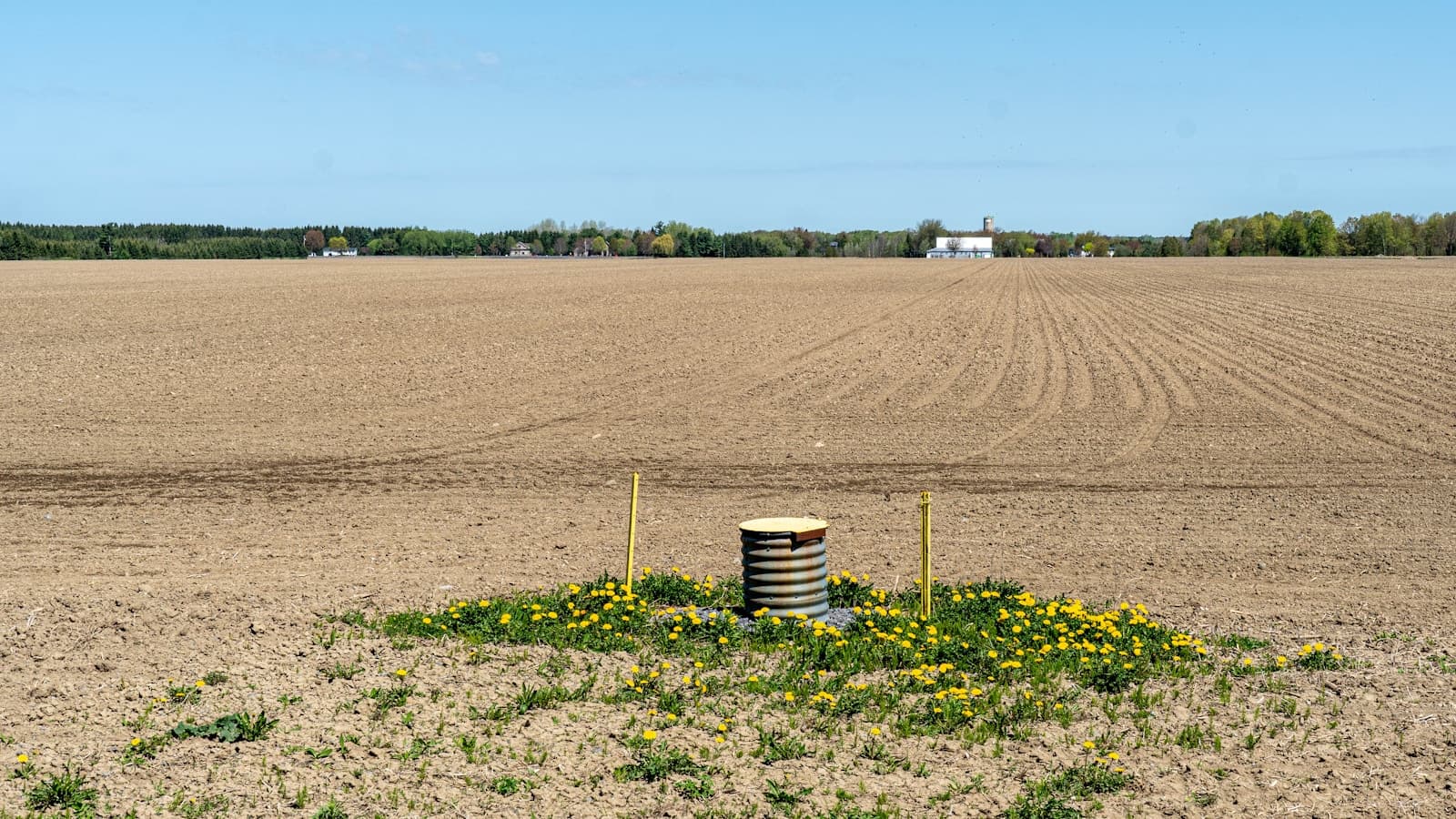 A modern corrugated-metal well casing sticking out of a plowed agricultural field.