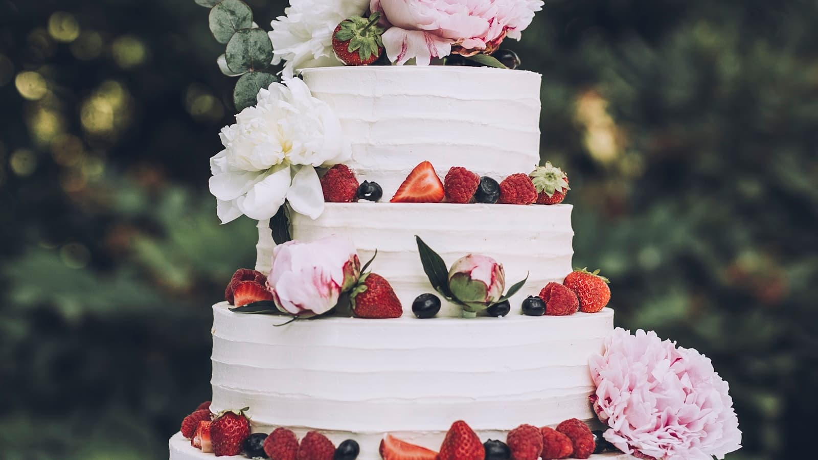A white wedding cake adorned with fresh strawberries and flowers.