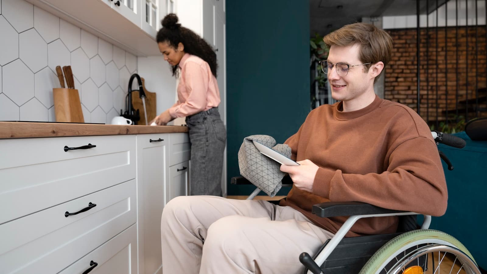 A man in a wheelchair using a tablet in a bright modern kitchen.