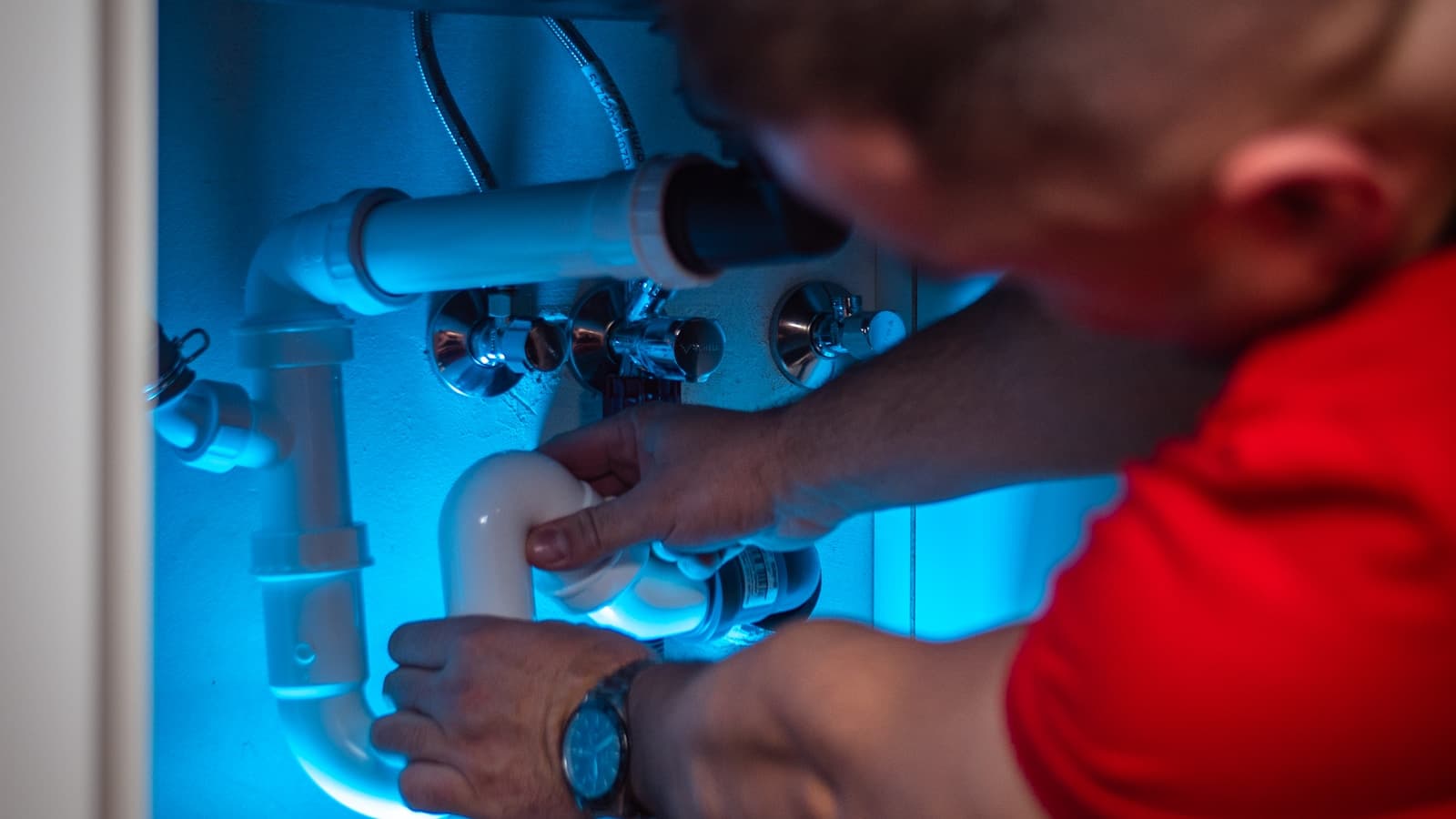 A plumber working on pipe fittings in a cabinet.