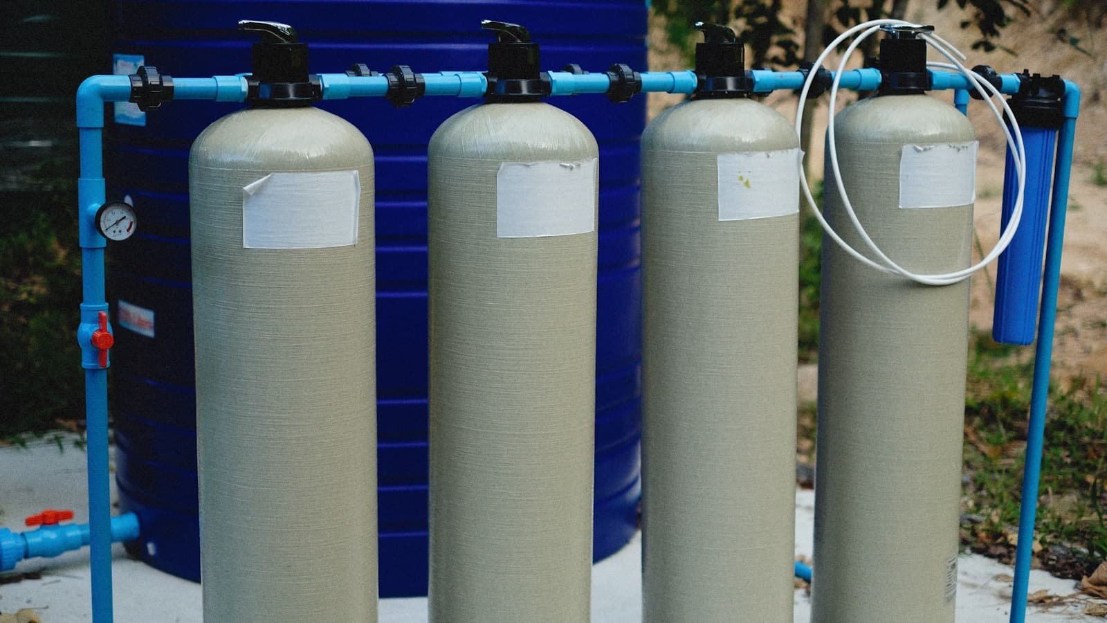 A row of water-softener tanks outdoors with blue piping.