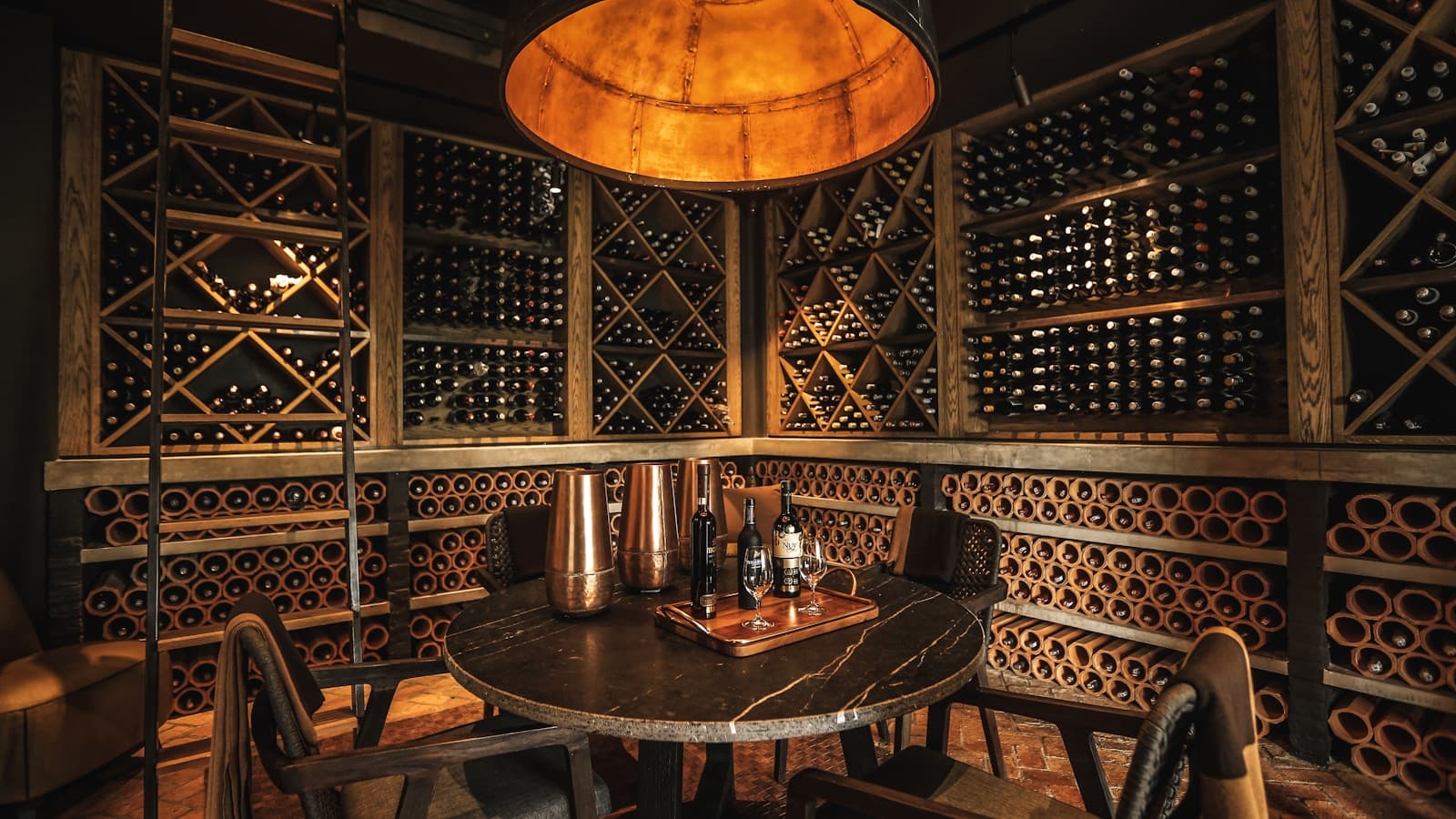 An elegant home wine cellar with diamond racks, a round tasting table, and pendant lamp.