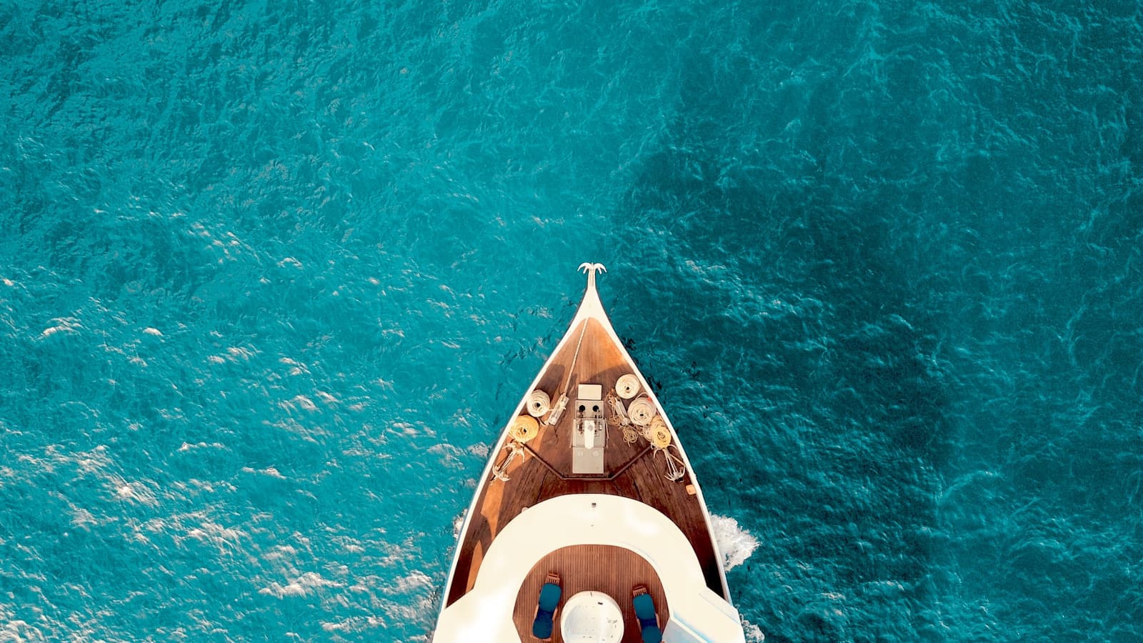 Aerial view of a yacht's bow cutting through turquoise water.