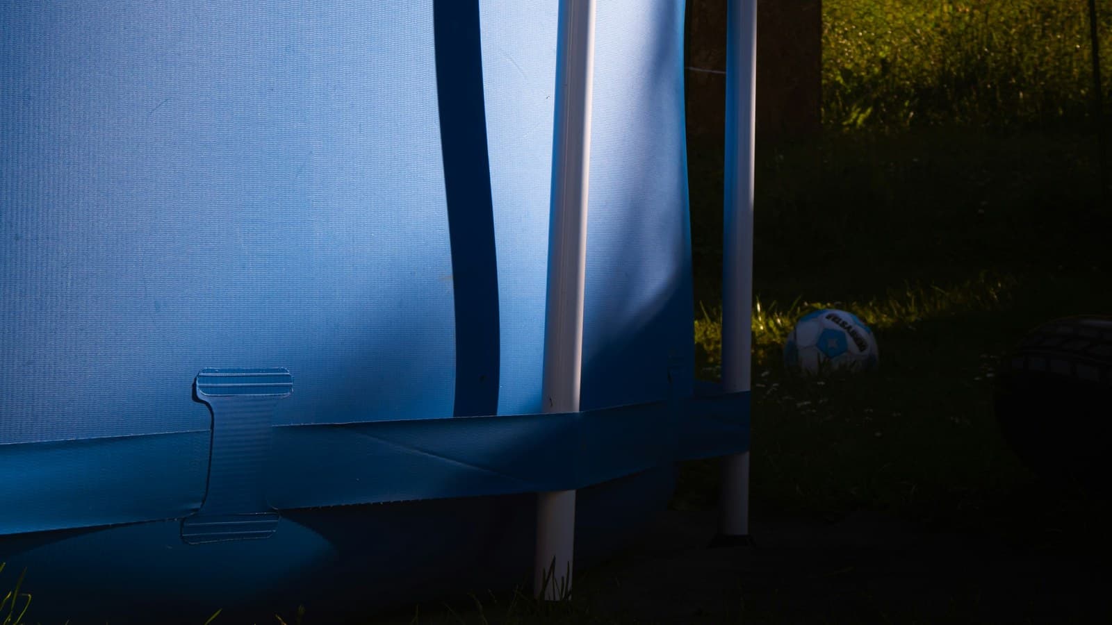 The blue vinyl wall of an above-ground pool in a backyard, with a soccer ball and grass nearby.