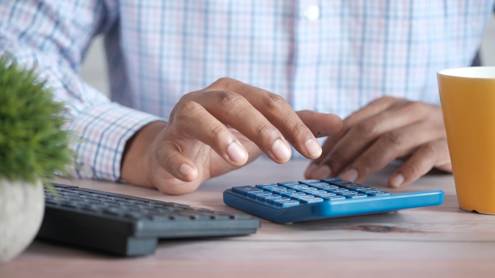 Close-up of hands using a calculator at a desk with a coffee mug.