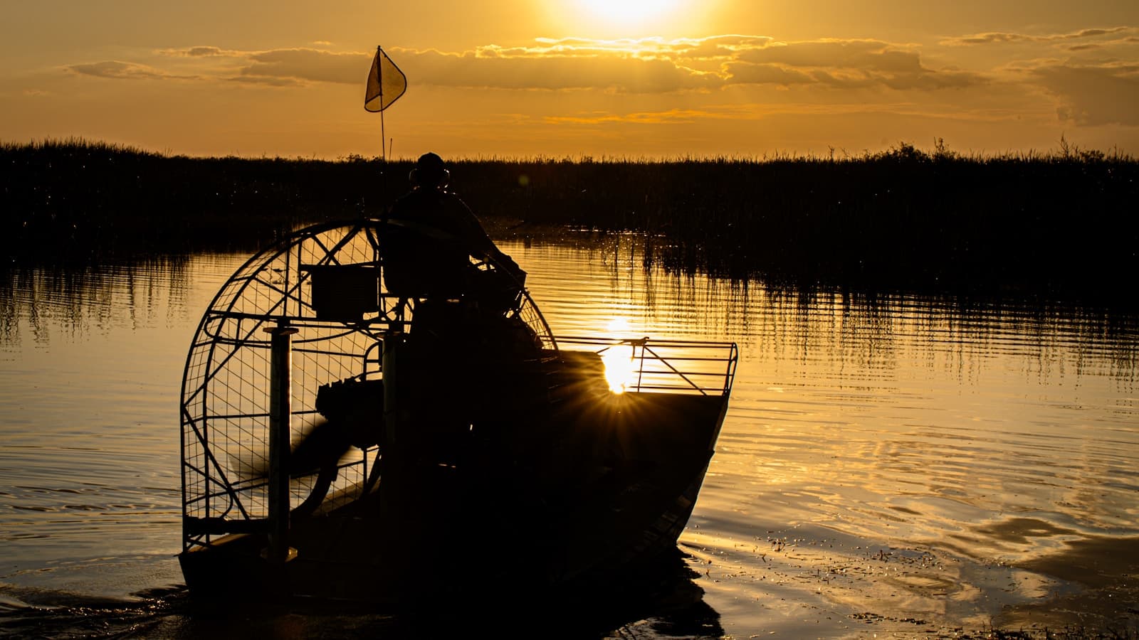 An airboat and rider in full silhouette against an orange sunset.
