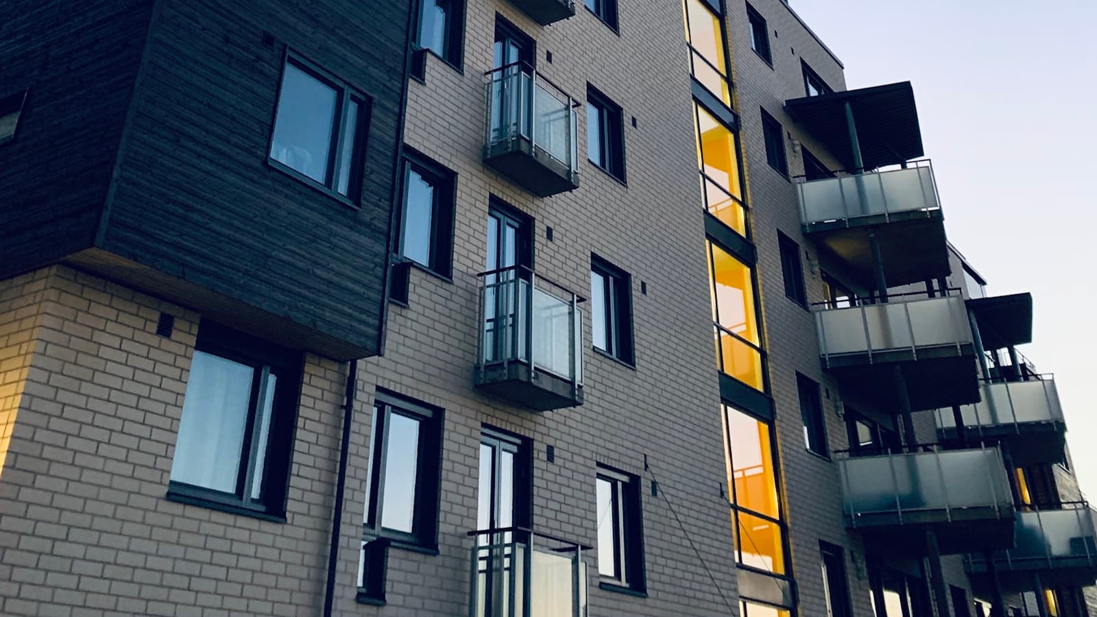 A low-angle exterior shot of a mid-rise apartment building in Oslo with brick and light facade, small balconies, and a clear sky.