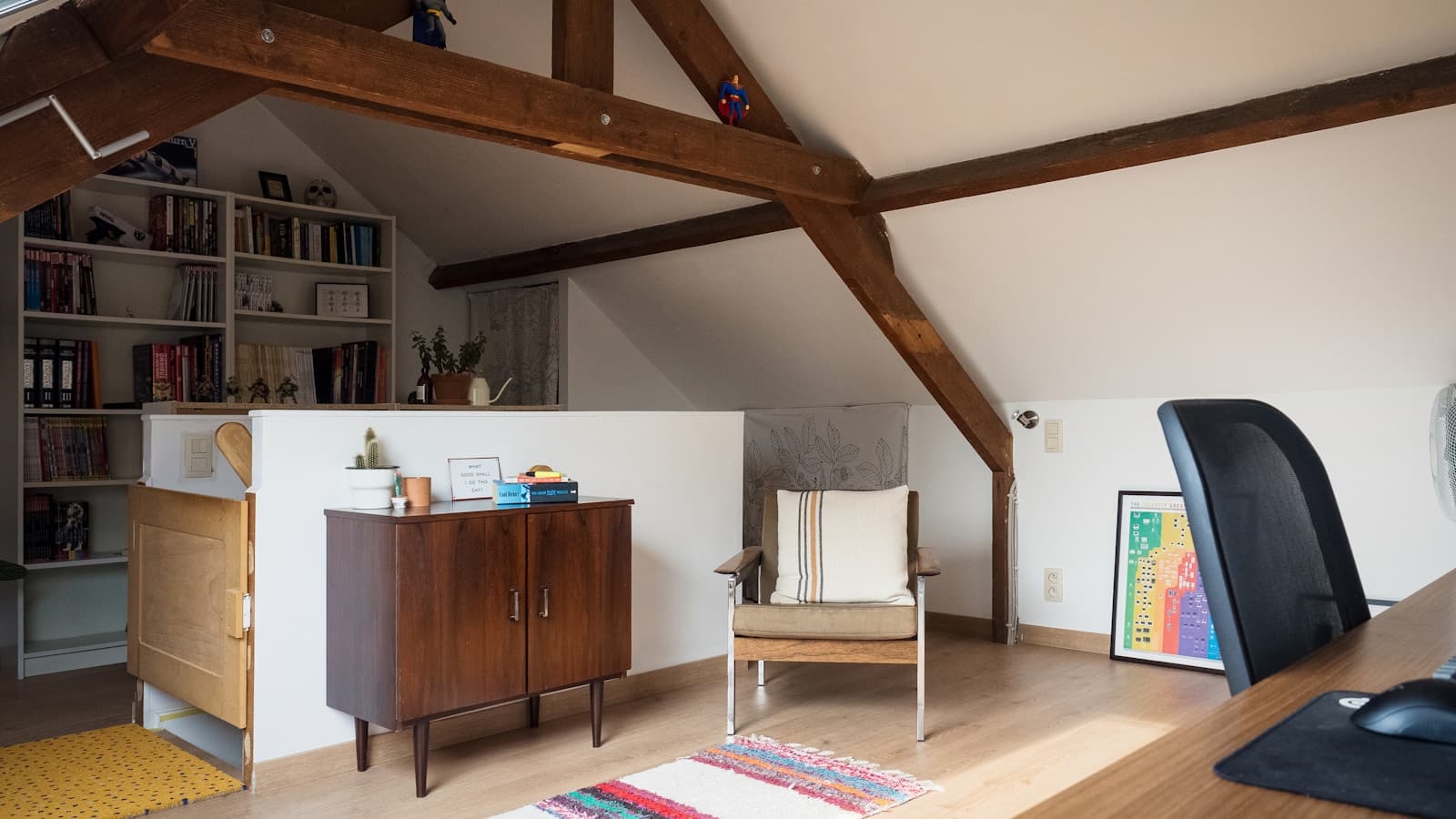 A finished attic home office with a sloped ceiling, exposed wood beams, bookshelves, and a desk.