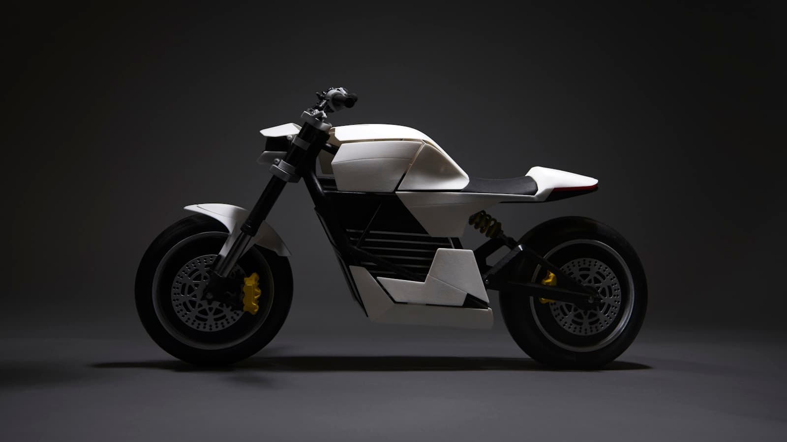 A sleek white and black modern-styled electric motorcycle photographed in a dark studio setting, with no text, plate, or people visible.