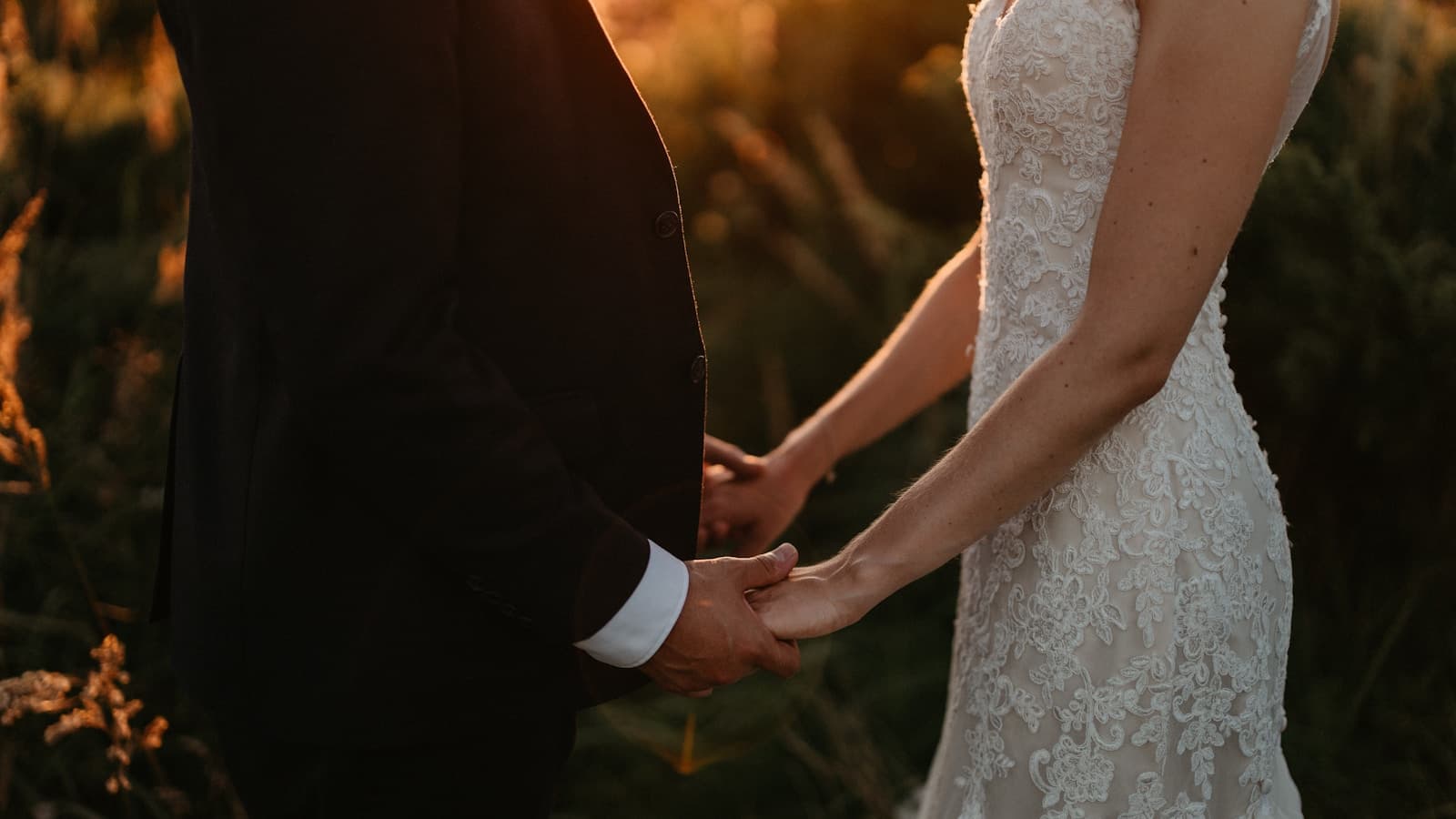 A bride and groom holding hands as the sun sets.