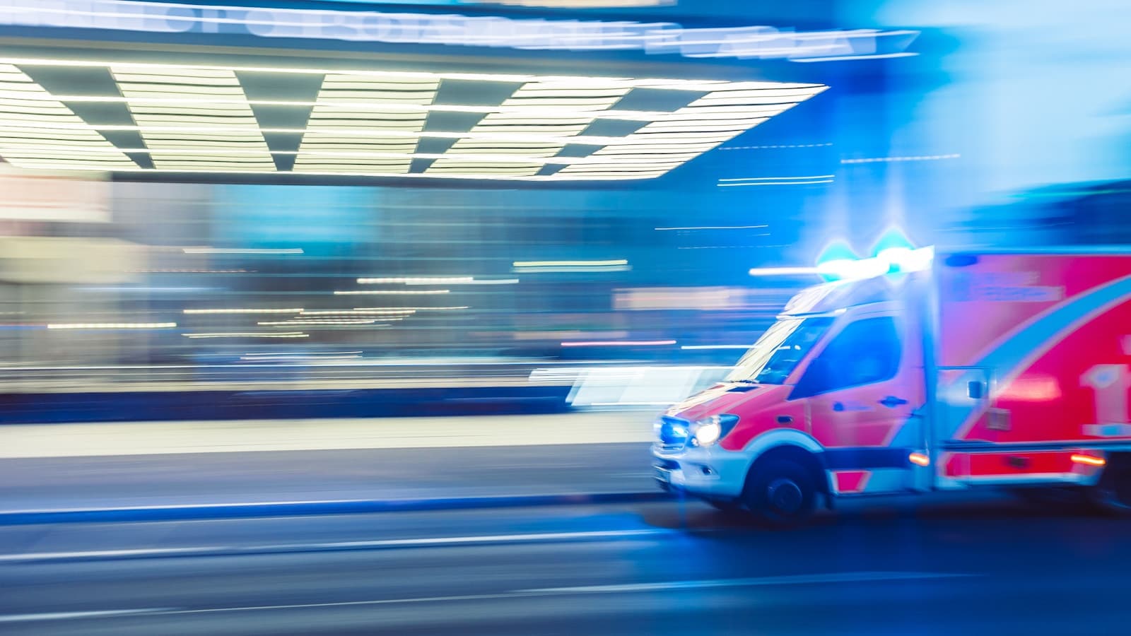 A modern ambulance in motion at night with blue emergency lights.