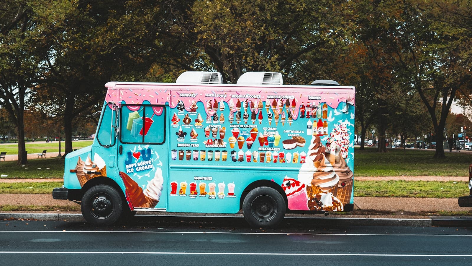 A brightly colored ice cream truck parked roadside in daylight.