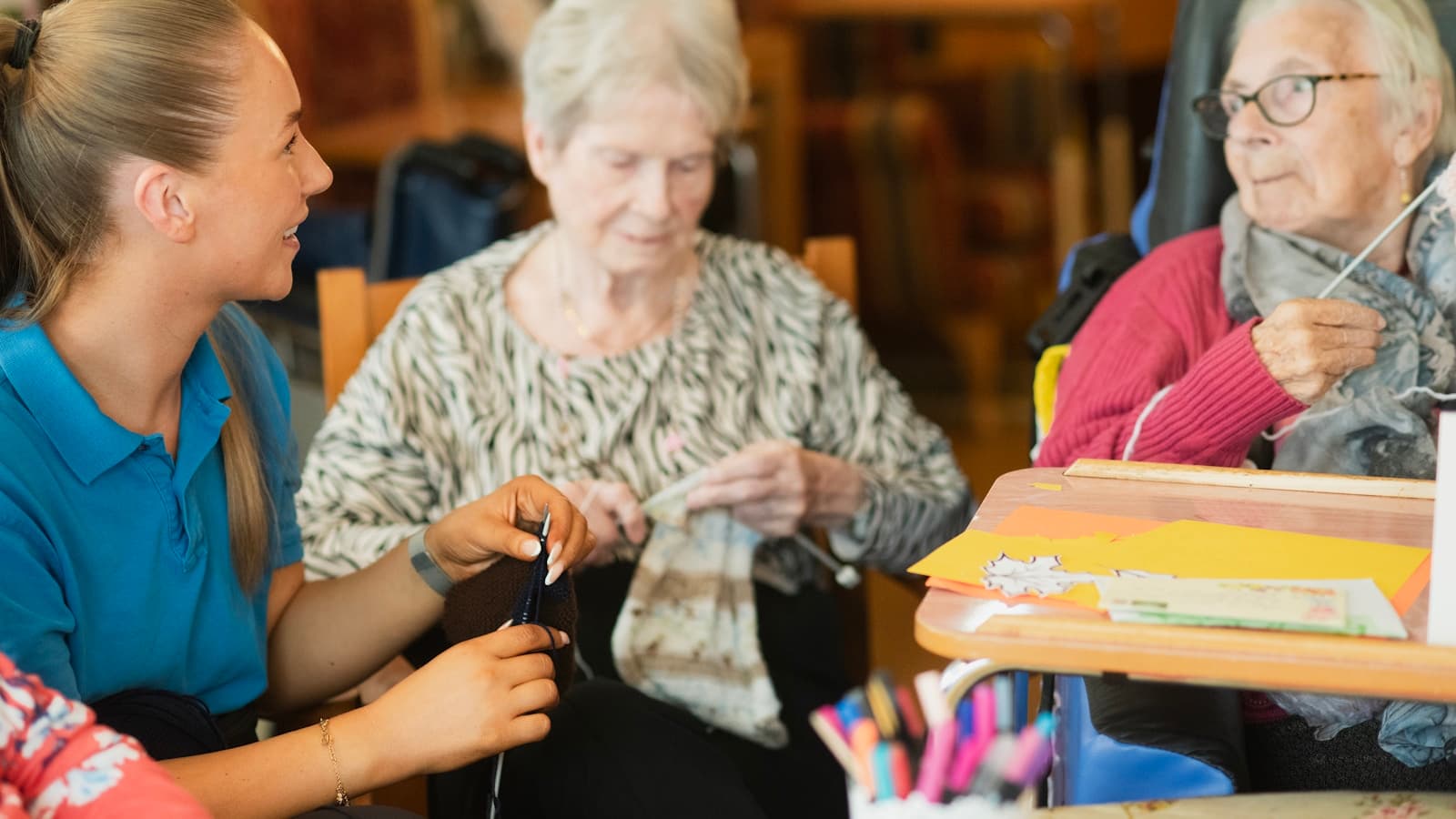 Close-up of a caregiver and two elderly women doing a knitting activity together.