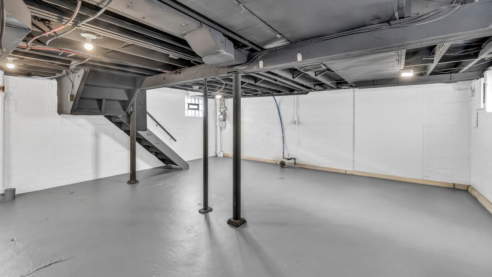 A spacious unfinished basement with support poles and a painted concrete floor.