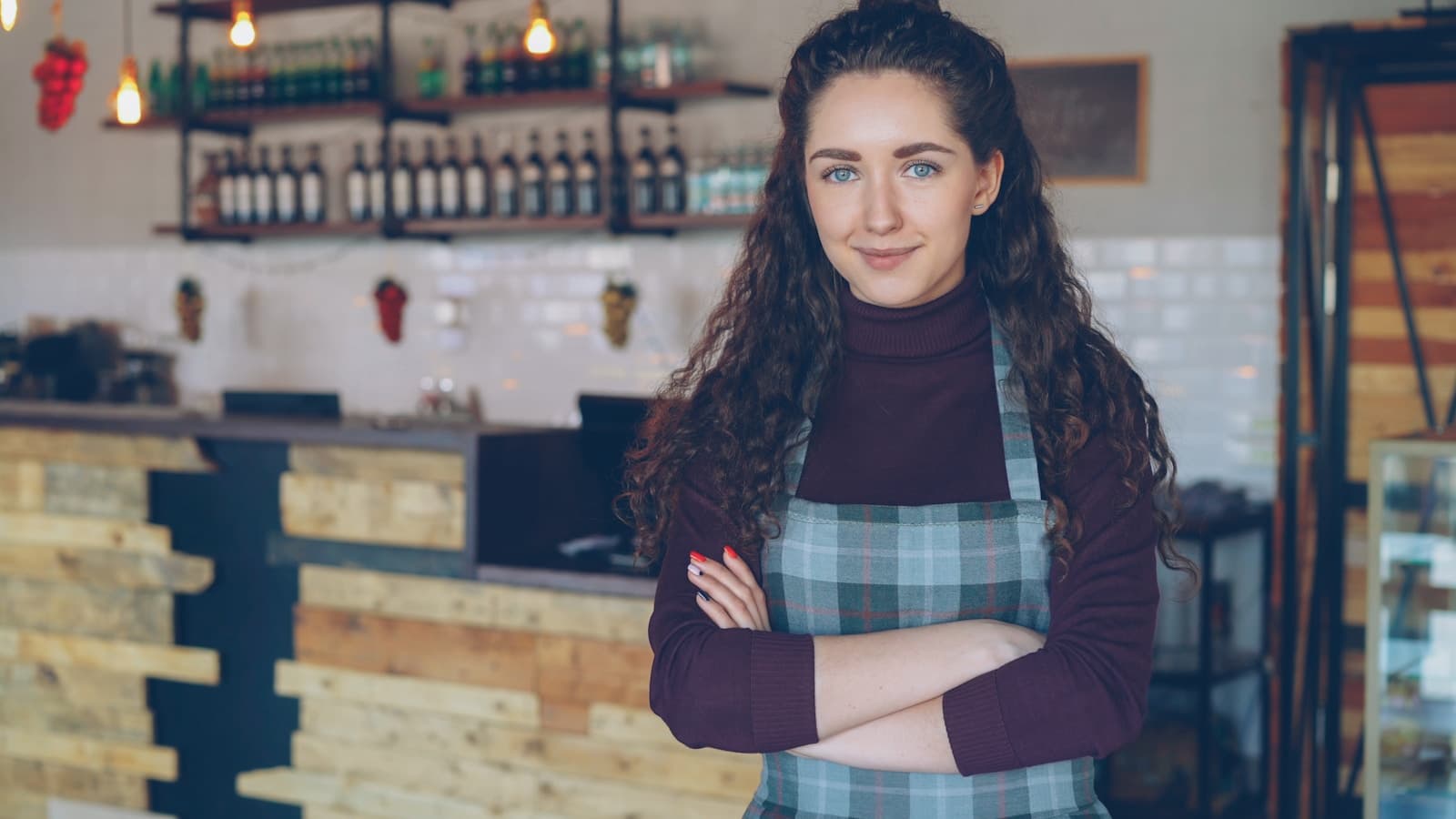 A smiling female shop owner standing confidently in her cafe, arms crossed.