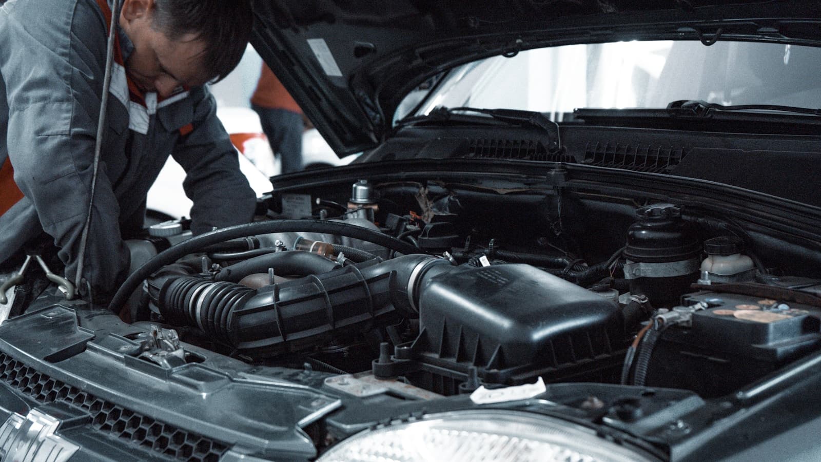A mechanic examining the engine bay of a car with the hood up, no visible badges or plates.